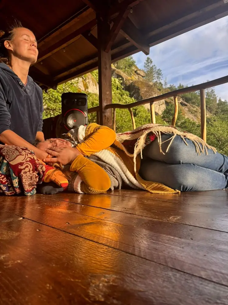 A guest resting wrapped in a blanket while a facilitator gently holds their hands