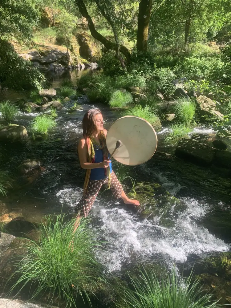 A woman playing a frame drum barefoot in the river