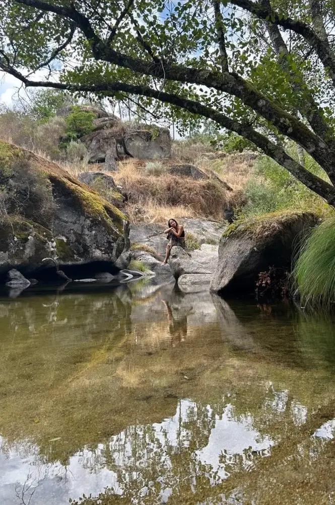 A woman sitting alone on a rock above a still river pool